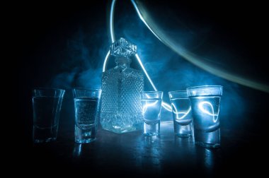 A beautiful carafe with vodka stands on a wooden table with glasses. Dramatic toned foggy background with light. Selective focus. Club drink concept.