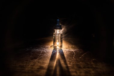 Vape konsepti. Karanlık arka planda duman bulutları ve tüp sıvısı şişeleri. Işık efektleri. Arka plan, vape reklamı ya da vape arkaplan olarak kullanışlı. Seçici odak
