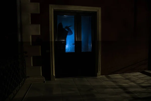 Silhouette of an unknown shadow figure on a door through a closed glass door. The silhouette of a human in front of a window at night. Scary scene halloween concept of blurred silhouette of maniac.