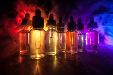 Vape konsepti. Karanlık arka planda duman bulutları ve tüp sıvısı şişeleri. Işık efektleri. Arka plan, vape reklamı ya da vape arkaplan olarak kullanışlı. Seçici odak