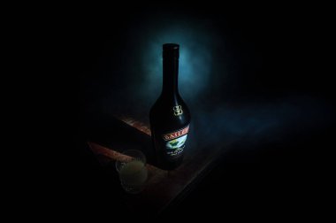 BAKU, AZERBAIJAN - FEB 09, 2020: Baileys Irish Cream is an Irish whiskey- and cream-based liqueur, made by Gilbeys of Ireland. A bottle of liqueur on wooden table with dark toned foggy background.