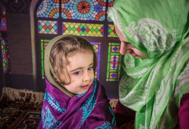 Müslüman anne kızına camide Kur 'an okumayı öğretiyor. Müslüman kadın ve küçük kız halının üzerinde oturuyor..