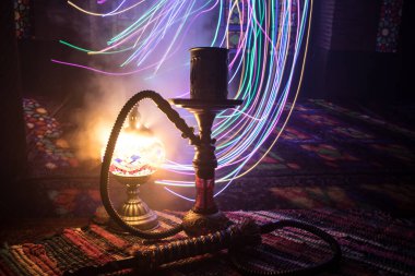 Shisha kasesinde sıcak nargile kömürleri Arap iç kısımlarında buhar bulutları oluşturuyor. Halıdaki doğulu süsü. Karanlıkta arka planda şık bir doğulu shisha..