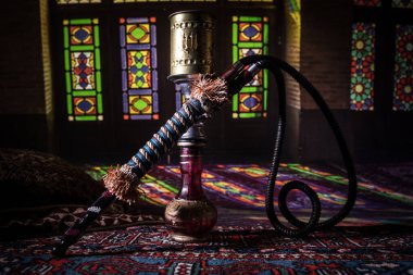Shisha kasesinde sıcak nargile kömürleri Arap iç kısımlarında buhar bulutları oluşturuyor. Halıdaki doğulu süsü. Karanlıkta arka planda şık bir doğulu shisha..