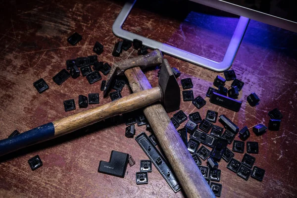 Broken keyboard with hammer on wooden table. Destroyed keyboard. An image of computer frustration