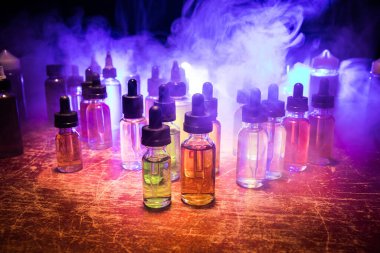 Vape konsepti. Karanlık arka planda duman bulutları ve tüp sıvısı şişeleri. Işık efektleri. Arka plan, vape reklamı ya da vape arkaplan olarak kullanışlı. Seçici odak