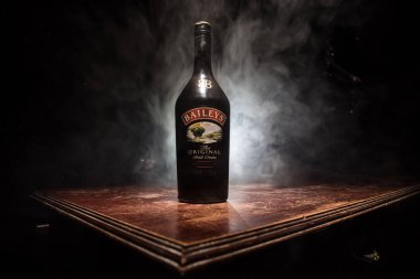 BAKU, AZERBAIJAN - FEB 09, 2020: Baileys Irish Cream is an Irish whiskey- and cream-based liqueur, made by Gilbeys of Ireland. A bottle of liqueur on wooden table with dark toned foggy background.