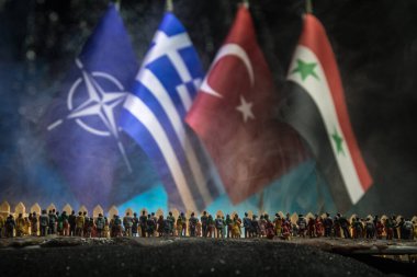 Yaratıcı ölçek dekorasyonu. Sınırda bekleyen Suriyeli mülteciler (kalabalık) Yunanistan, Nato, Suriye ve Türkiye bayrağına bakıyor. Savaş krizi kavramı. Seçici odak