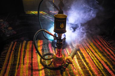 Shisha kasesinde sıcak nargile kömürleri Arap iç kısımlarında buhar bulutları oluşturuyor. Halıdaki doğulu süsü. Karanlıkta arka planda şık bir doğulu shisha..