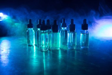 Vape konsepti. Karanlık arka planda duman bulutları ve tüp sıvısı şişeleri. Işık efektleri. Arka plan, vape reklamı ya da vape arkaplan olarak kullanışlı. Seçici odak