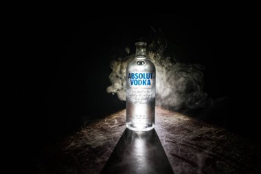 BAKU, AZERBAIJAN - FEB 09, 2020: Absolut Vodka is a brand of vodka, produced near Ahus, in Sweden. Owned by French group Pernod Ricard. Bottle of vodka on wooden table with dark toned foggy background.
