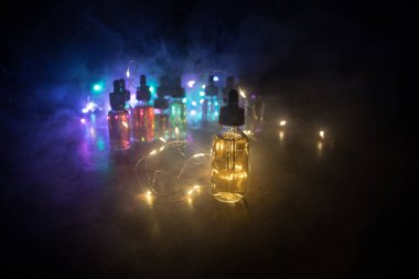 Vape konsepti. Karanlık arka planda duman bulutları ve tüp sıvısı şişeleri. Işık efektleri. Arka plan, vape reklamı ya da vape arkaplan olarak kullanışlı. Seçici odak