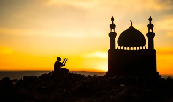 Concept of religion Islam. Silhouette of man praying on the background of a mosque at sunset. Festive greeting card, invintation for Muslim Holiday