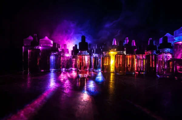 Vape konsepti. Karanlık arka planda duman bulutları ve tüp sıvısı şişeleri. Işık efektleri. Arka plan, vape reklamı ya da vape arkaplan olarak kullanışlı. Seçici odak