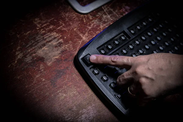 Broken keyboard with hammer on wooden table. Keyboard with no keys on dark desktop. Woman finger on ESC button. Only one workable button on keyboard