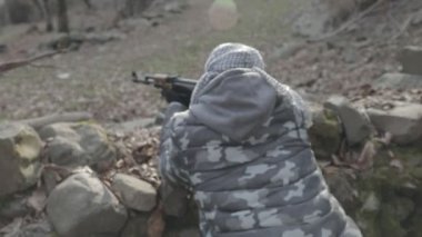 Maskeli ve tüfekli bir adam ormana saldırmaya hazır. Silah doğrultan tehlikeli bir haydut. Dağ yolundaki askeri harekat sırasında özel asker..