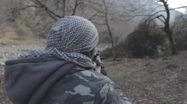 Maskeli ve tüfekli bir adam ormana saldırmaya hazır. Silah doğrultan tehlikeli bir haydut. Dağ yolundaki askeri harekat sırasında özel asker..