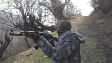 Maskeli ve tüfekli bir adam ormana saldırmaya hazır. Silah doğrultan tehlikeli bir haydut. Dağ yolundaki askeri harekat sırasında özel asker..