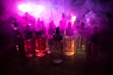 Vape konsepti. Karanlık arka planda duman bulutları ve tüp sıvısı şişeleri. Işık efektleri. Arka plan, vape reklamı ya da vape arkaplan olarak kullanışlı. Seçici odak