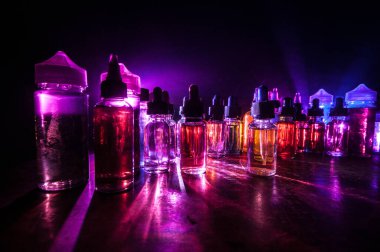 Vape konsepti. Karanlık arka planda duman bulutları ve tüp sıvısı şişeleri. Işık efektleri. Arka plan, vape reklamı ya da vape arkaplan olarak kullanışlı. Seçici odak