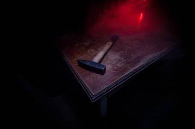 Koyu tonlu sisli bir arka planda, ahşap bir masanın üzerinde eski model bir çekiç. Seçici odak.