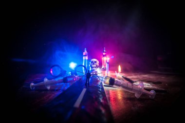 Narcotic drug problem concept. Silhouette of a man standing in the middle of the road on a misty night with giant Drug syringe and narcotic attributes. Creative artwork decoration