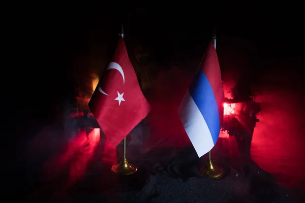 Closeup, flags of Russia and Turkey against destroyed city at night. Decorated diorama. Concept of crisis of war and political conflicts between nations. Selective focus