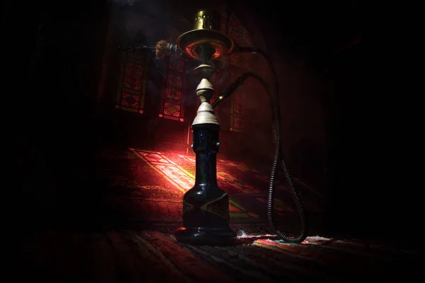 Hookah hot coals on shisha bowl making clouds of steam at Arabian interior. Oriental ornament on the carpet. Stylish oriental shisha in dark with backlight.