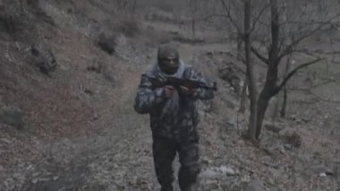 Maskeli ve tüfekli bir adam ormana saldırmaya hazır. Silah doğrultan tehlikeli bir haydut. Dağ yolundaki askeri harekat sırasında özel asker..