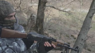 Maskeli ve tüfekli bir adam ormana saldırmaya hazır. Silah doğrultan tehlikeli bir haydut. Dağ yolundaki askeri harekat sırasında özel asker..