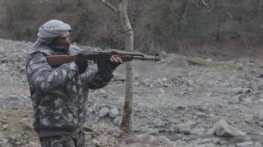 Maskeli ve tüfekli bir adam ormana saldırmaya hazır. Silah doğrultan tehlikeli bir haydut. Dağ yolundaki askeri harekat sırasında özel asker..