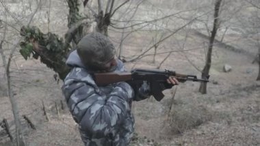 Maskeli ve tüfekli bir adam ormana saldırmaya hazır. Silah doğrultan tehlikeli bir haydut. Dağ yolundaki askeri harekat sırasında özel asker..