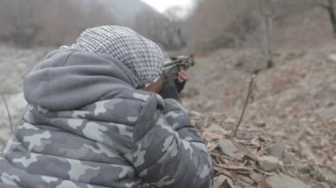 Maskeli ve tüfekli bir adam ormana saldırmaya hazır. Silah doğrultan tehlikeli bir haydut. Dağ yolundaki askeri harekat sırasında özel asker..