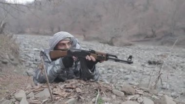 Maskeli ve tüfekli bir adam ormana saldırmaya hazır. Silah doğrultan tehlikeli bir haydut. Dağ yolundaki askeri harekat sırasında özel asker..