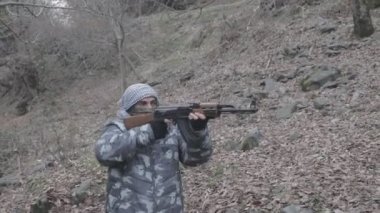 Maskeli ve tüfekli bir adam ormana saldırmaya hazır. Silah doğrultan tehlikeli bir haydut. Dağ yolundaki askeri harekat sırasında özel asker..