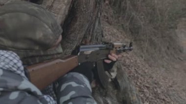 Maskeli ve tüfekli bir adam ormana saldırmaya hazır. Silah doğrultan tehlikeli bir haydut. Dağ yolundaki askeri harekat sırasında özel asker..