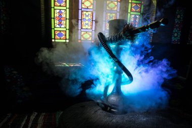 Shisha kasesinde sıcak nargile kömürleri Arap iç kısımlarında buhar bulutları oluşturuyor. Halıdaki doğulu süsü. Karanlıkta arka planda şık bir doğulu shisha..