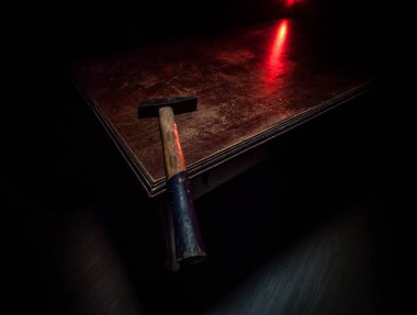 Koyu tonlu sisli bir arka planda, ahşap bir masanın üzerinde eski model bir çekiç. Seçici odak.