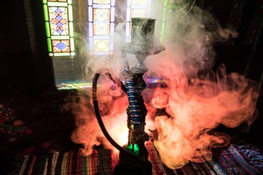 Shisha kasesinde sıcak nargile kömürleri Arap iç kısımlarında buhar bulutları oluşturuyor. Halıdaki doğulu süsü. Karanlıkta arka planda şık bir doğulu shisha..