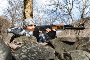 Maskeli ve tüfekli bir adam ormana saldırmaya hazır. Silah doğrultan tehlikeli bir haydut. Dağ yolundaki askeri operasyon sırasında özel bir askerdi. Seçici odak