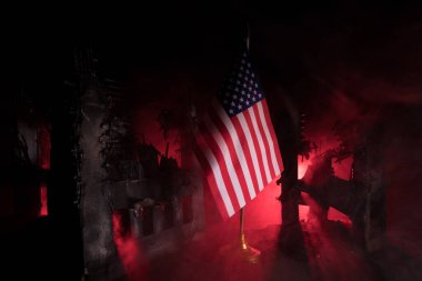 Closeup, flag of USA against destroyed city at night. Decorated diorama. Concept of crisis of war and political conflicts between nations. Selective focus clipart