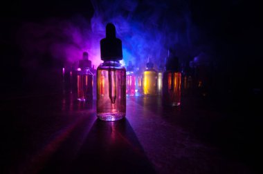 Vape konsepti. Karanlık arka planda duman bulutları ve tüp sıvısı şişeleri. Işık efektleri. Arka plan, vape reklamı ya da vape arkaplan olarak kullanışlı. Seçici odak
