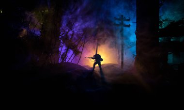 Büyük kalibreli tüfekli ordu keskin nişancısı ateş ve dumanın içinde duruyor. Savaş Konsepti. Savaş sahnesi sisli gökyüzü arka planında geceleri Bulutlu Skyline 'ın altında siluetlerle savaşmak. Şehir savaş yüzünden yok oldu.