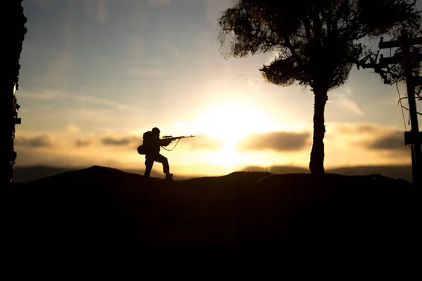 Army sniper with large caliber rifle standing in the fire and smoke. War Concept. Battle scene on war fog sky background, Fighting silhouettes Below Cloudy Skyline at sunset. City destroyed by war