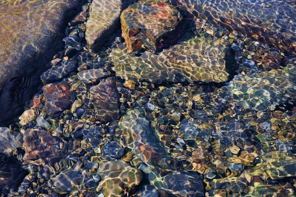 Yaz güneşi su altındaki nehir taşlarında güzel desenler yaratır. Doğa çekimi.