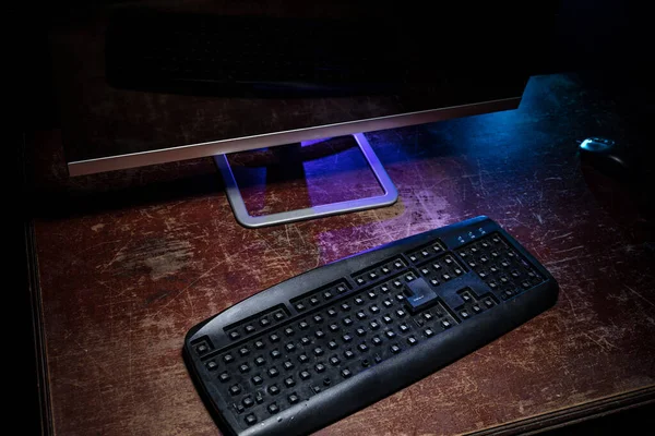 Broken keyboard with hammer on wooden table. Keyboard with no keys on dark desktop.