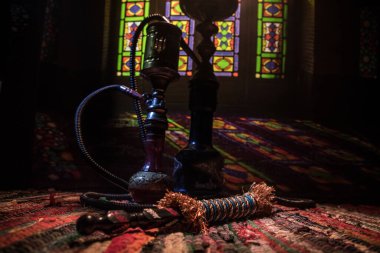 Shisha kasesinde sıcak nargile kömürleri Arap iç kısımlarında buhar bulutları oluşturuyor. Halıdaki doğulu süsü. Karanlıkta arka planda şık bir doğulu shisha..