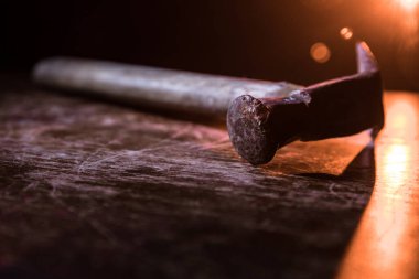 Koyu tonlu sisli bir arka planda, ahşap bir masanın üzerinde eski model bir çekiç. Seçici odak.