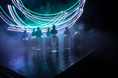 Vape konsepti. Karanlık arka planda duman bulutları ve tüp sıvısı şişeleri. Işık efektleri. Arka plan, vape reklamı ya da vape arkaplan olarak kullanışlı. Seçici odak
