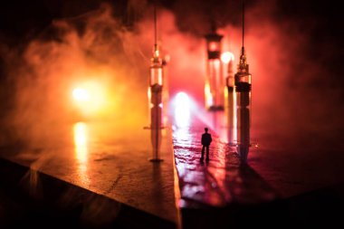 Narcotic drug problem concept. Silhouette of a man standing in the middle of the road on a misty night with giant Drug syringe and narcotic attributes. Creative artwork decoration